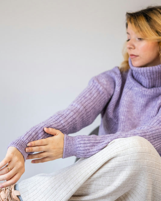 a woman in a purple sweater and white pants