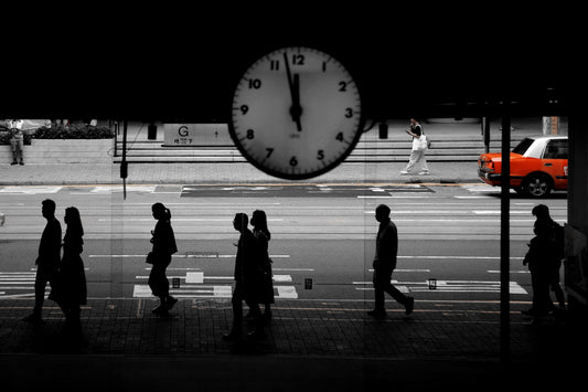 People walk by a clock on a busy street.