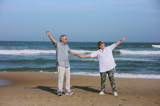 Elderly couple holding hands on a sandy beach.